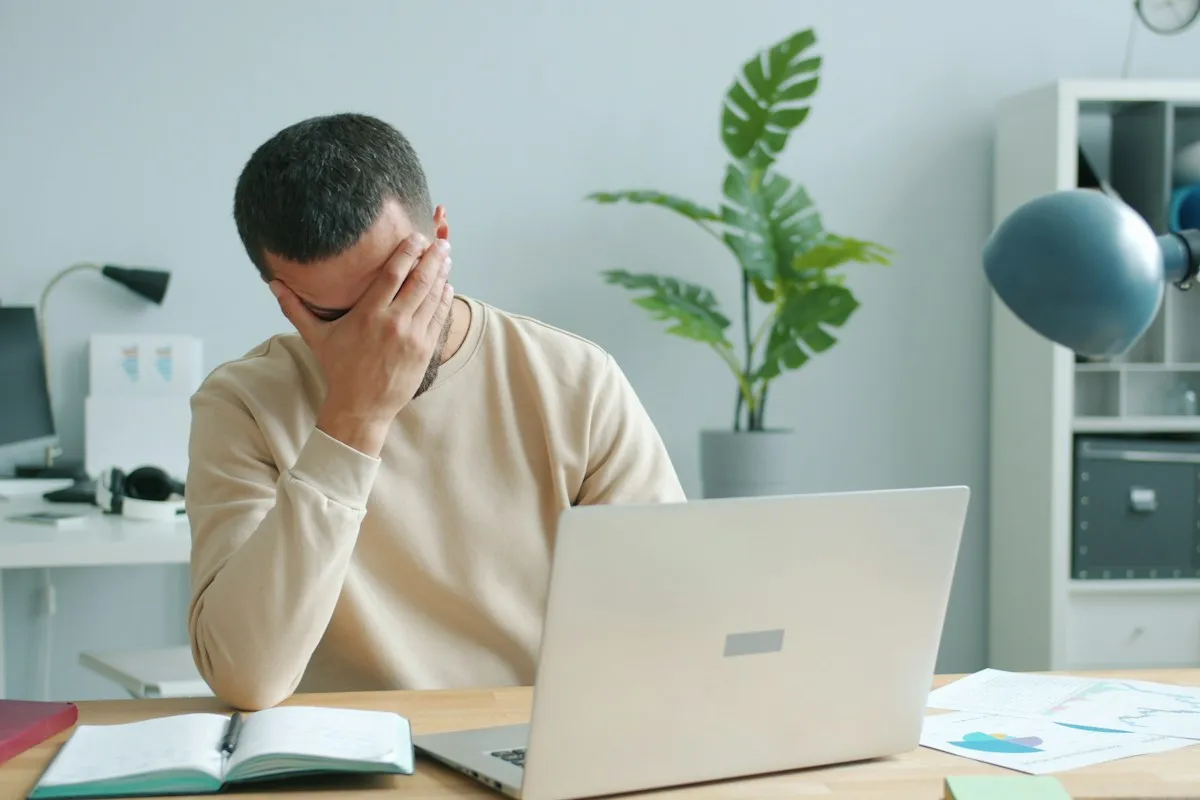 Mann am Schreibtisch hält sich die Hand vor die Augen, vor ihm ein aufgeklappter Laptop