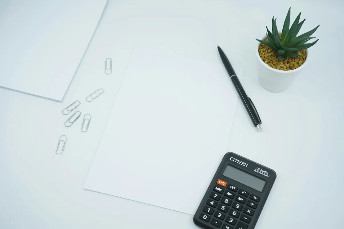 Taschenrechner, Stift und leeres Papier auf einem hellen Schreibtisch