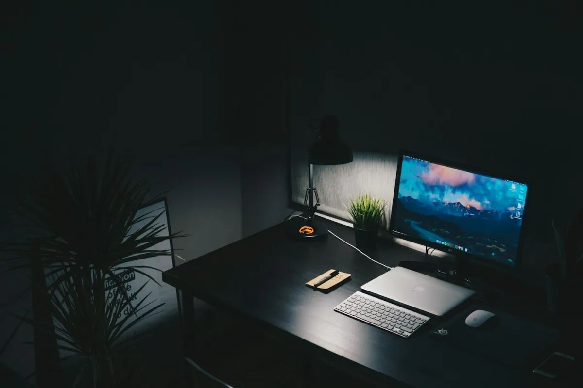 Schreibtisch mit Monitor und Tastatur in einem abgedunkelten Raum
