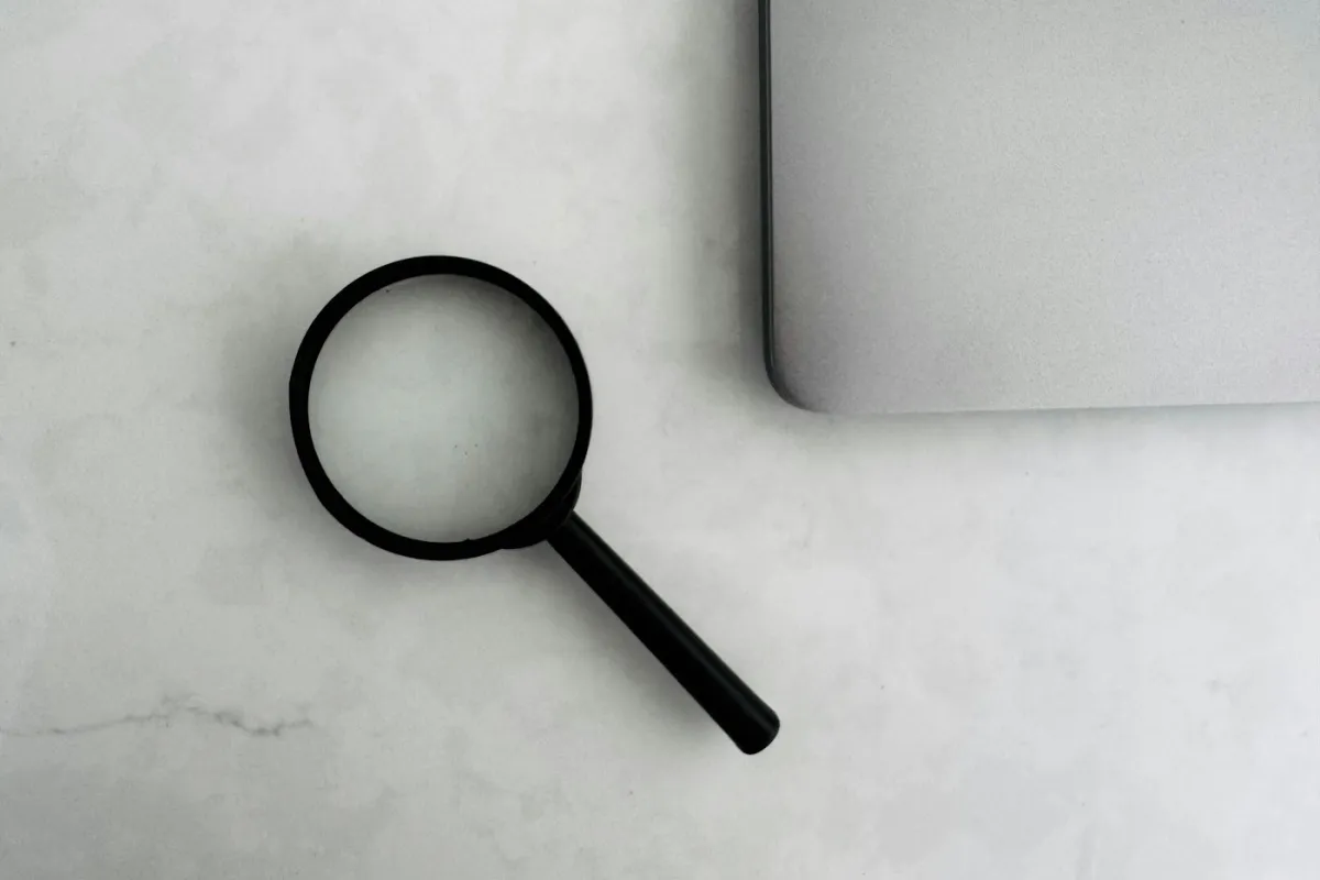 Lupe neben einem zugeklappten Laptop auf einer hellen Arbeitsfläche