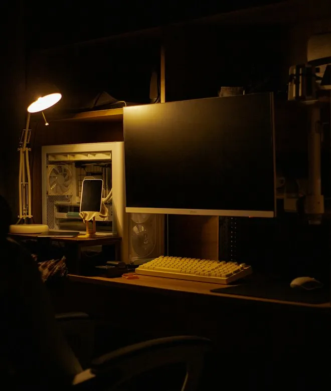 Schreibtisch mit Monitor und Tastatur, von einer Lampe beleuchtet: die Prüfung läuft von Hand und in Ruhe.