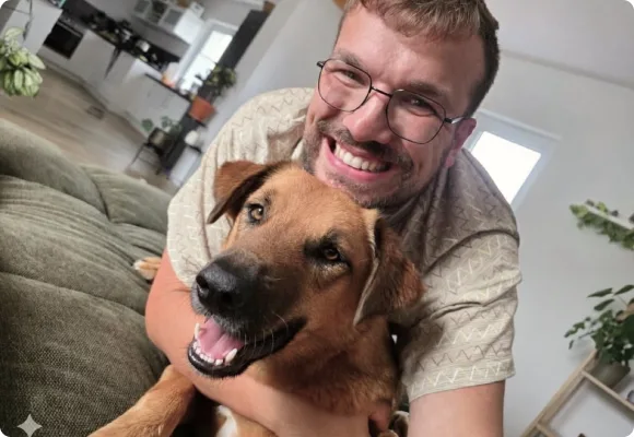 Dennis Theis auf dem Sofa, den Arm um seinen Hund Kaami gelegt.