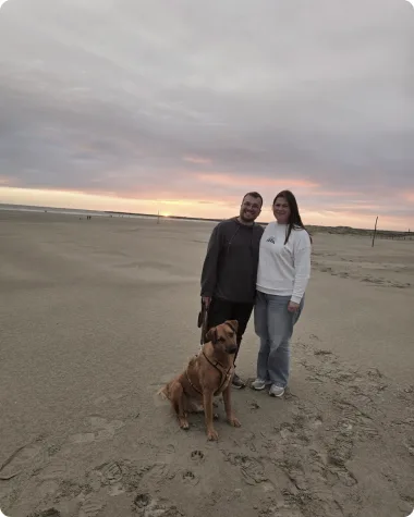 Christina, Kaami und Dennis Theis am Strand, im Hintergrund geht die Sonne unter.